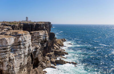 Rock formation in sea against clear blue sky