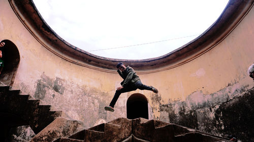 Low angle view of man jumping against building