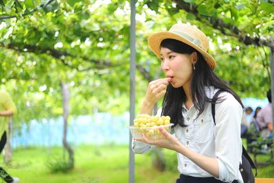 Young woman eating grapes against plants on field