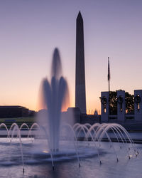 Fountain in city against sky during sunset