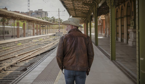 Rear view of adult man standing on platform in train station