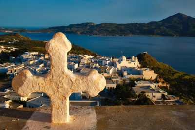 Christian cross and plaka village on milos island over red geranium flowers on sunset in greece