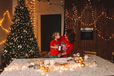 Cheerful parents and a child in red pajamas prepare christmas cookies in the decorated kitchen