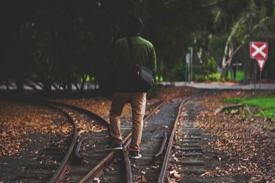 Rear view of man walking on railroad tracks