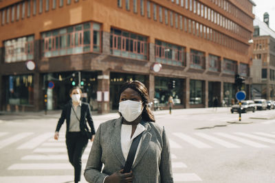 Female entrepreneurs crossing street on sunny day in city during covid-19