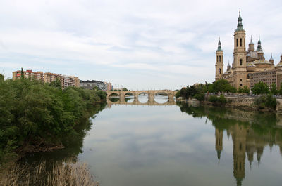 Arch bridge over river by buildings against sky