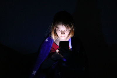 Young woman using phone while standing in dark room