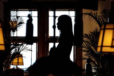 Silhouette woman standing by window at home