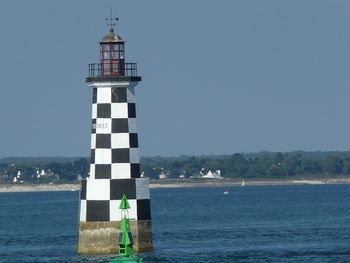 Lighthouse by sea against clear sky