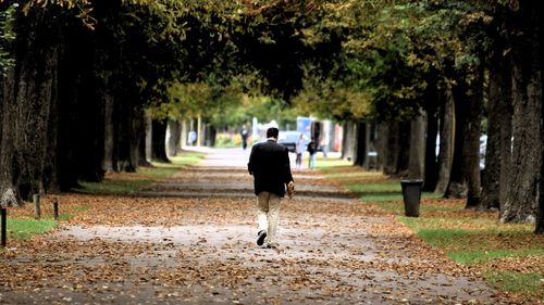 Rear view of man walking on road during autumn