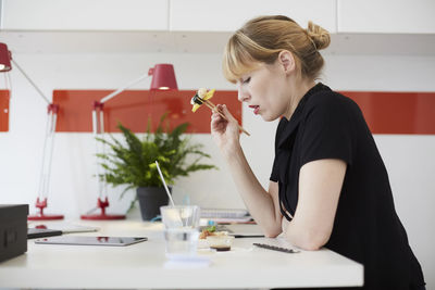 Side view of mid adult businesswoman eating lunch at table in office
