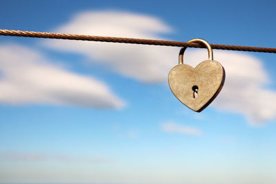 Close-up of heart shape padlock on cable against sky