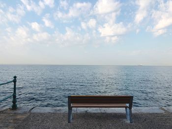 Empty bench by sea against sky