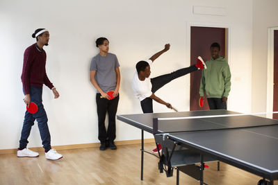 Boy showing stunt to friends while playing table tennis in games room