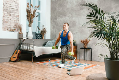 The athlete makes lunges in the bedroom, in the background there is a bed, a vase, a carpet.