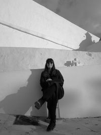 Full length of smiling woman sitting on chair outside church against wall