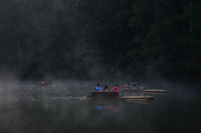 People on wooden raft at lake against trees