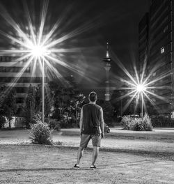 Rear view of man walking on illuminated street at night