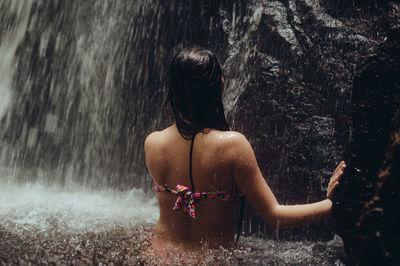 Rear view of sensuous young woman standing in river against waterfall