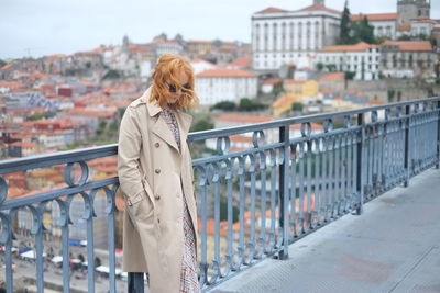 Thoughtful woman standing by railing on bridge in city