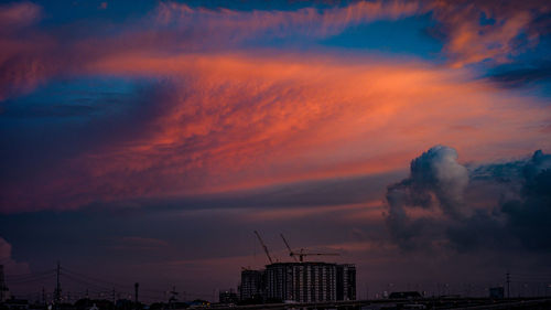 Silhouette buildings against dramatic sky during sunrise