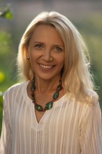 A beautiful fifty-year-old woman with light hair, dressed in white clothing and stone bead necklaces