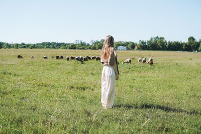 Rear view of woman standing on grassy field against clear sky