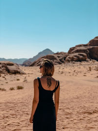 Rear view of woman standing in desert against clear sky