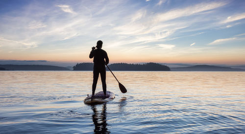 Silhouette man standing in sea against sky during sunset