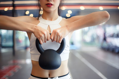 Midsection of woman holding kettlebell while exercising in gym