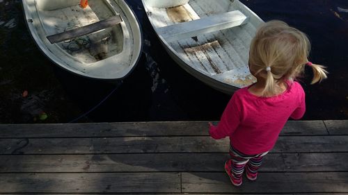 Rear view of girl standing on pier against boats moored in river