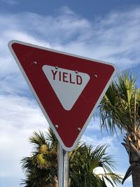 Yield sign with blue sky and palm trees behind it