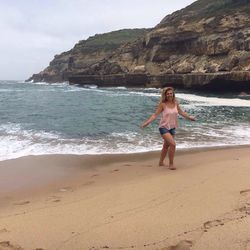 Happy woman walking on shore against rock formation