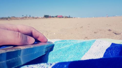 Close-up of hands on sand against clear sky