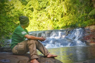 Man sitting by waterfall