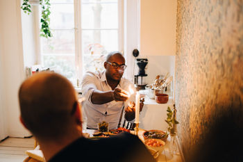 Man lighting candle while sitting with friend during dinner party at table