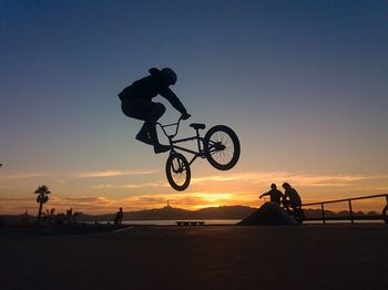 Silhouette man practicing stunt with bicycle against sky during sunset