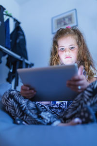 Cute girl using digital tablet while sitting on bed at home