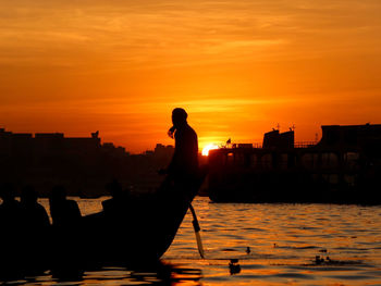 Silhouette man standing by sea against orange sky during sunset