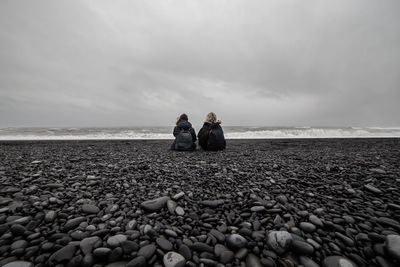 Women sitting at beach against sky