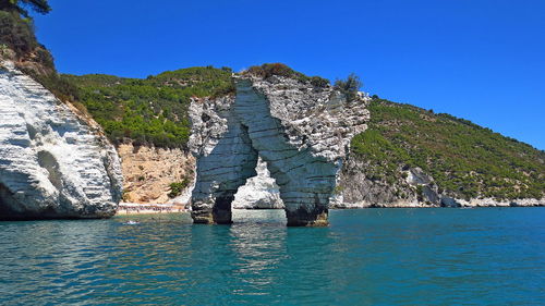 Rock formation against sea and clear blue sky