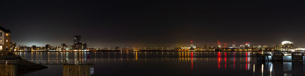 Illuminated buildings by sea against sky at night