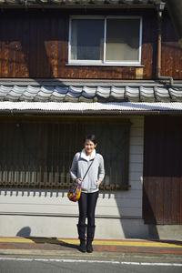 Young woman standing against house on sunny day