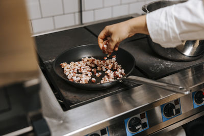 Female chef cooking diced meat in pan on stove at restaurant kitchen