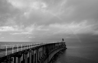 Pier over sea against rainbow in cloudy sky