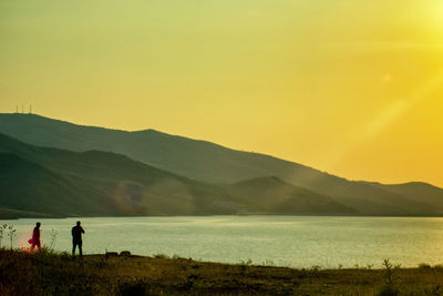 Silhouette people standing on land against sky during sunset
