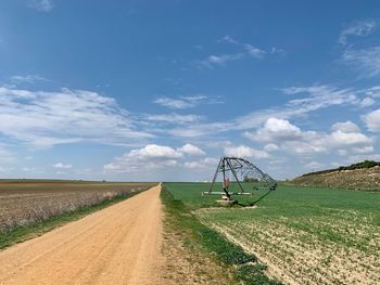Dirt road amidst agricultural field against sky