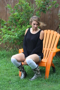 Fashionable young woman sitting on adirondack chair in yard