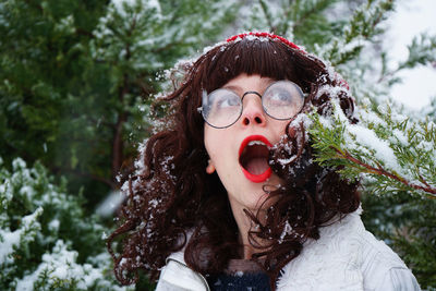 Close-up of young woman with mouth open against trees during winter