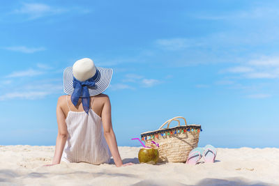 Rear view of woman sitting at beach against blue sky